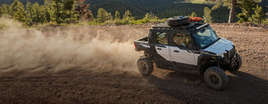 2027 Polaris XPEDITION XP five-seat with roof rack and spare tire kicking up dust on a mountain dirt trail