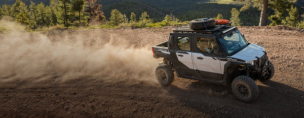 2027 Polaris XPEDITION XP five-seat with roof rack and spare tire kicking up dust on a mountain dirt trail