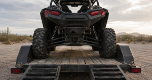 Side-by-side UTV loaded on an open deck trailer viewed from behind, showing how wheel offset affects clearance between the tires and the trailer fenders