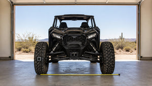 Sport side-by-side UTV parked head-on in an open garage on level concrete, with a tape measure laid across the ground between the front tires to check toe alignment
